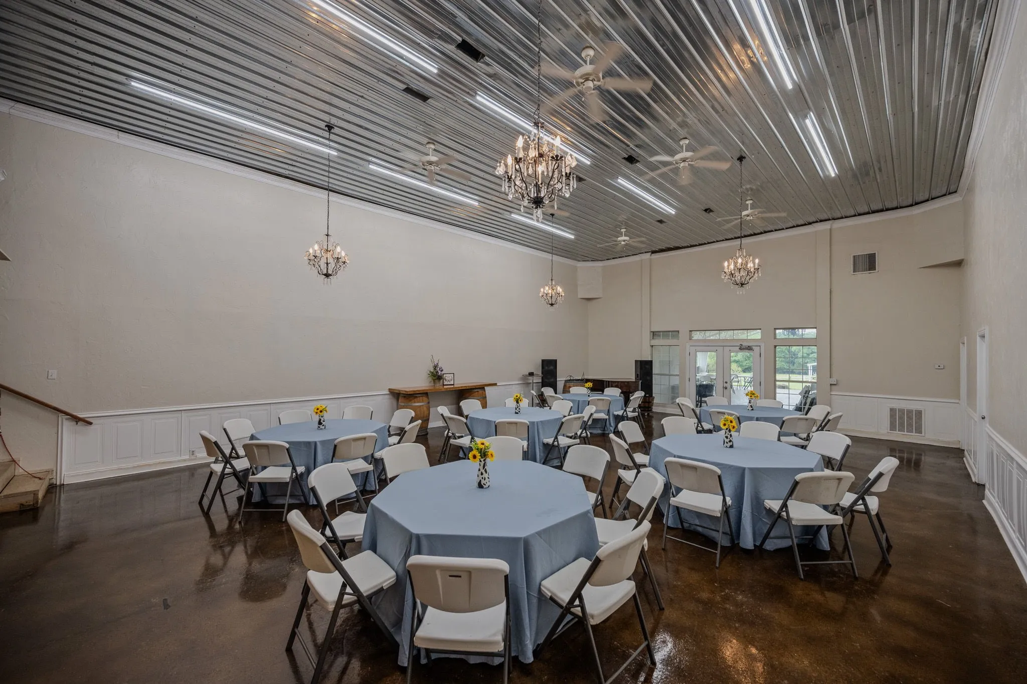 Spacious interior featuring a corrugated metal ceiling with integrated strip lighting, multiple ceiling fans, and chandelier fixtures