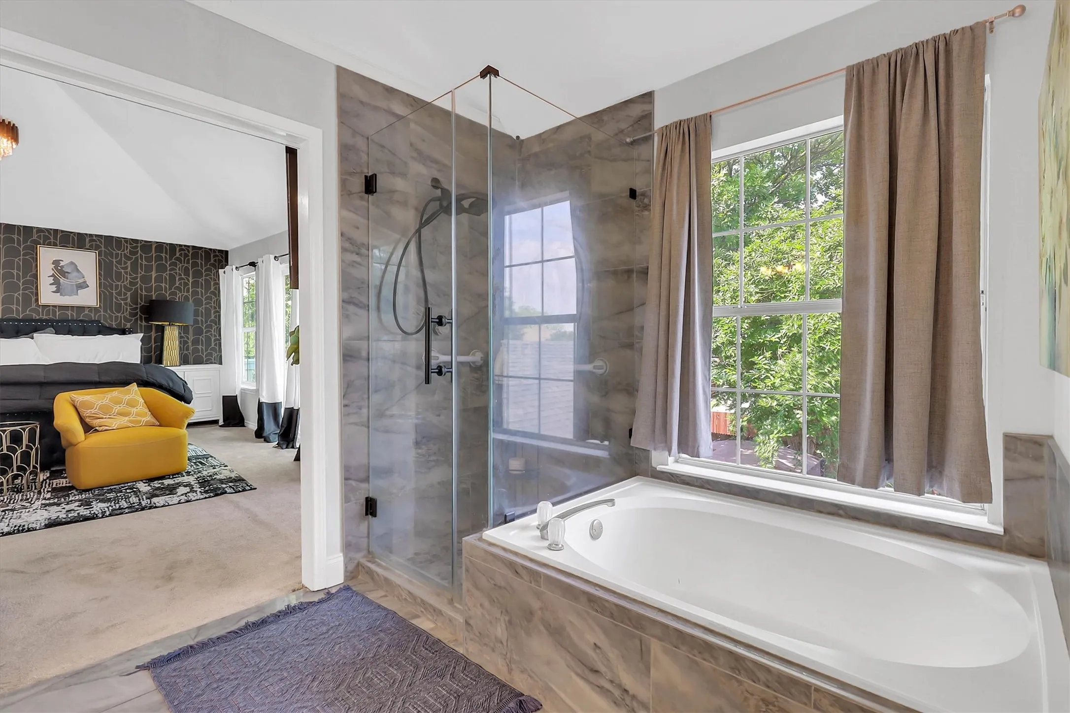 Soaking tub with a large window overlooking lush greenery, a frameless glass shower enclosure, and stone-finish wall paneling