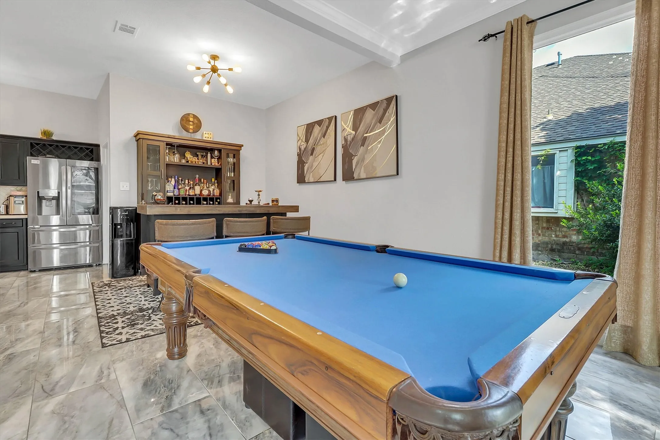 Game room featuring a billiard table with blue felt, a built-in bar with seating, and a full-size stainless steel refrigerator