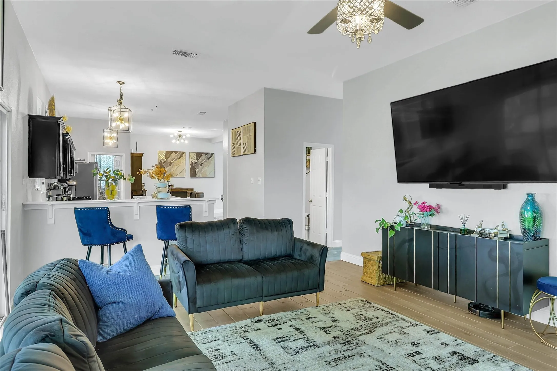 Open-concept living area featuring light wood-finish flooring, a contemporary ceiling fan with chandelier detailing, and a breakfast bar with built-in seating
