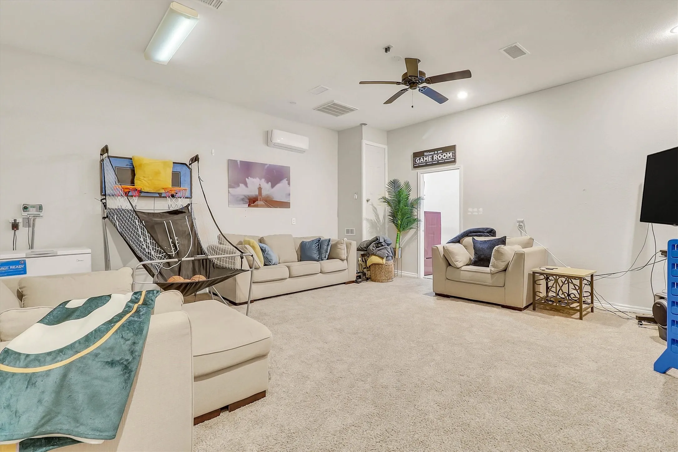Spacious carpeted room featuring a ceiling fan, wall-mounted air conditioning unit, and flush-mount lighting