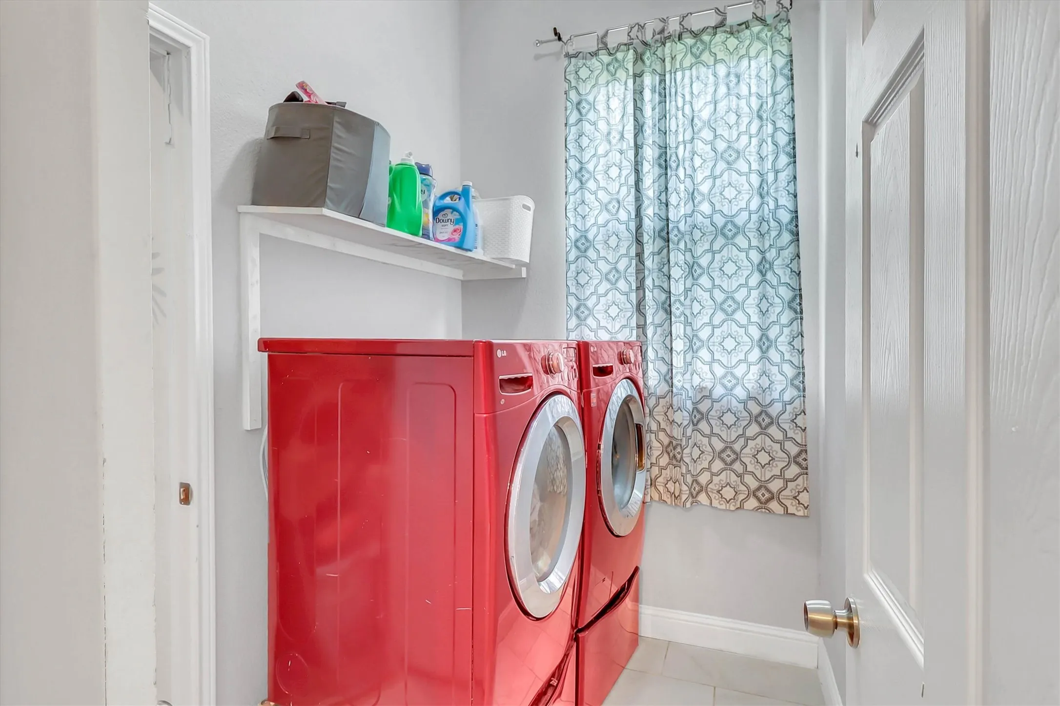 Laundry area featuring light gray walls, white trim, and a window with patterned curtains