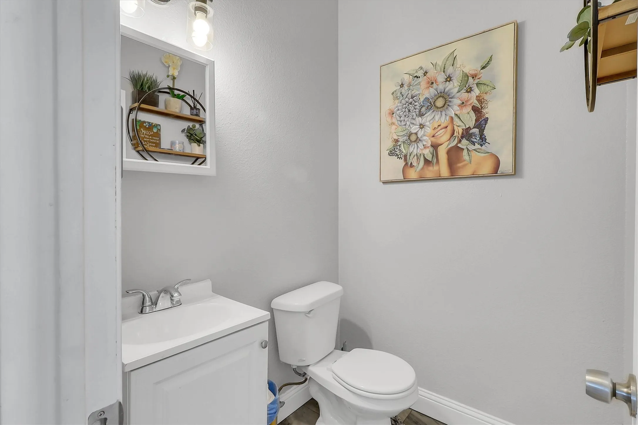 Powder room featuring a white single-sink vanity with chrome fixtures, a white toilet, recessed wall shelving with wood-finish accents, and wood-finish flooring