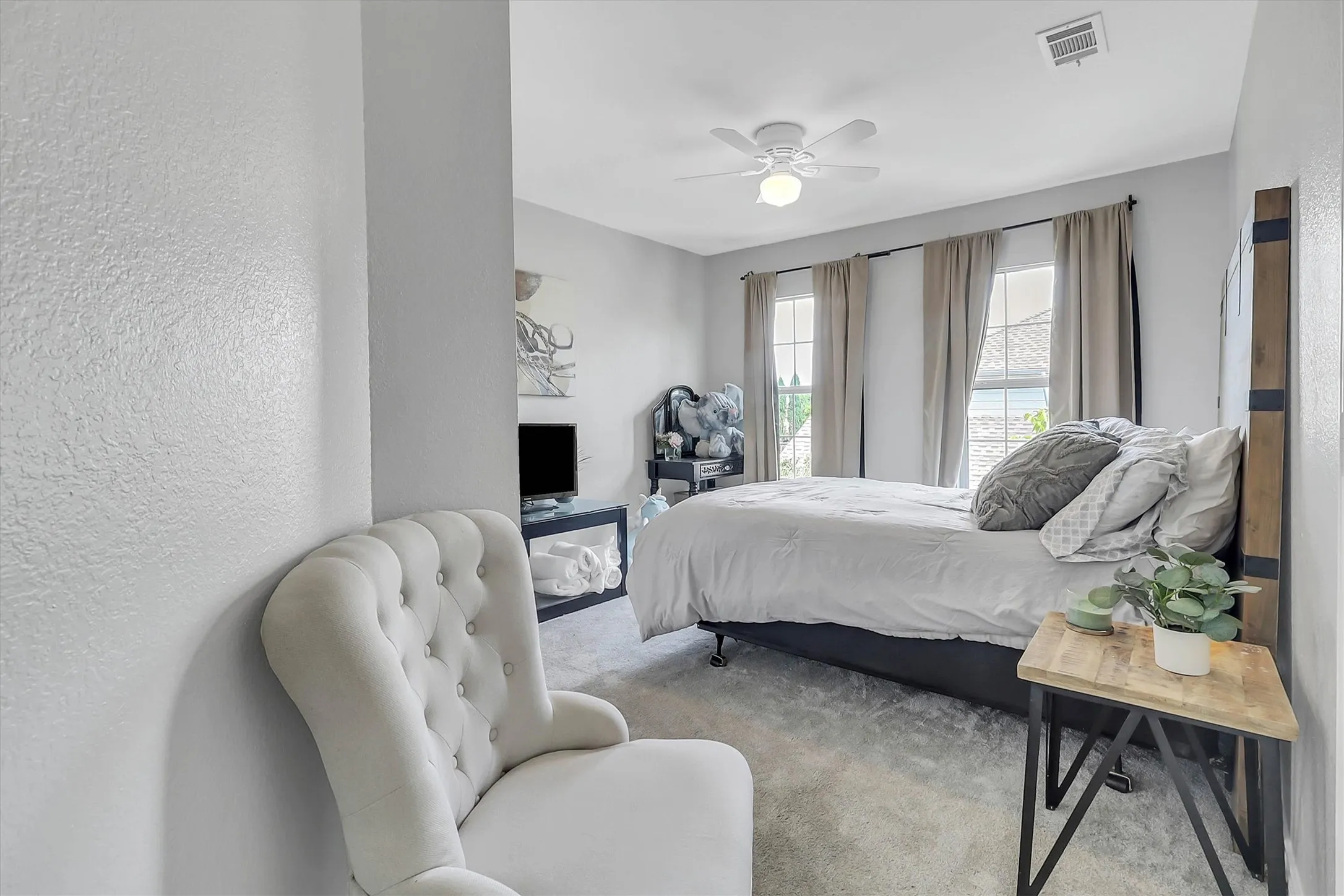 Carpeted bedroom featuring two large windows with drapes, a ceiling fan with integrated lighting, and light gray walls
