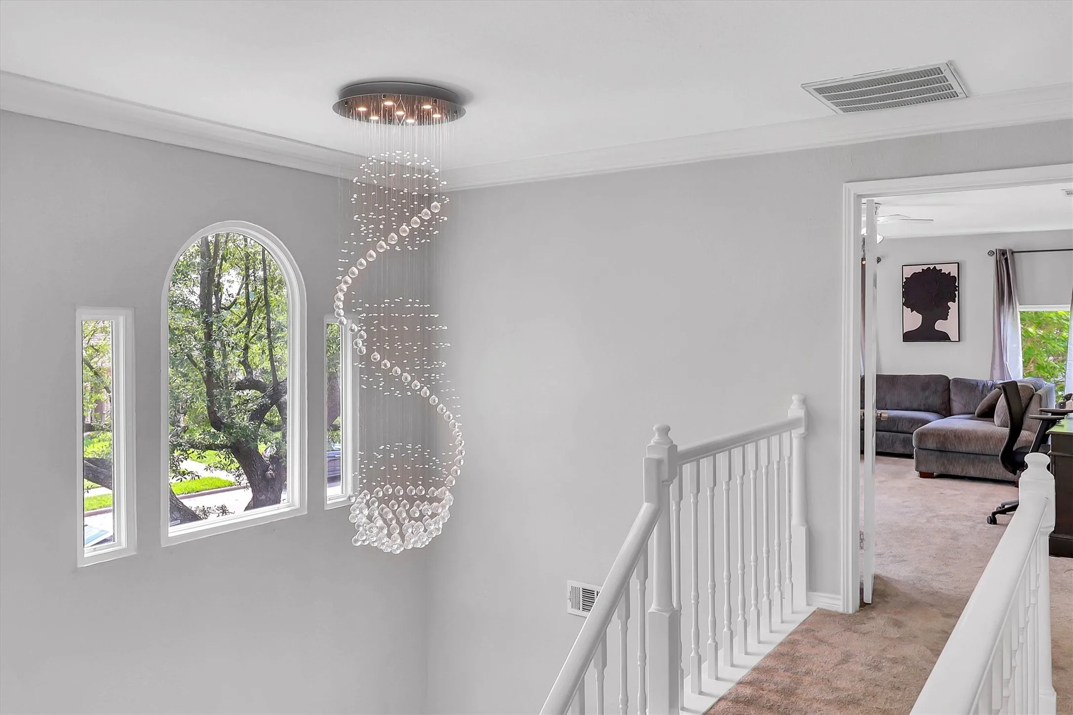Foyer landing with a tiered crystal chandelier, arched window, and two narrow vertical windows
