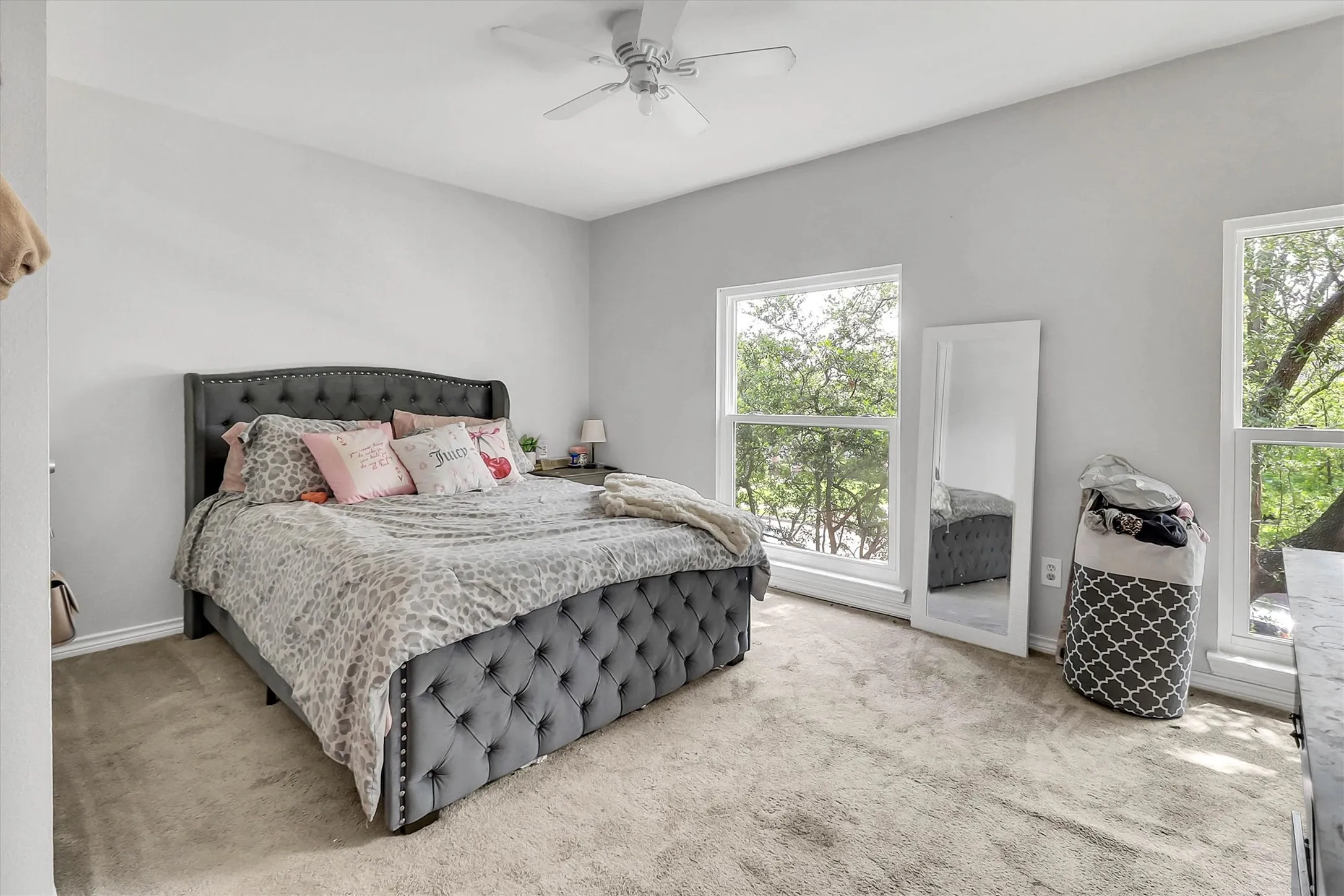 Spacious room featuring light gray walls, plush carpet flooring, two large windows, and a ceiling fan