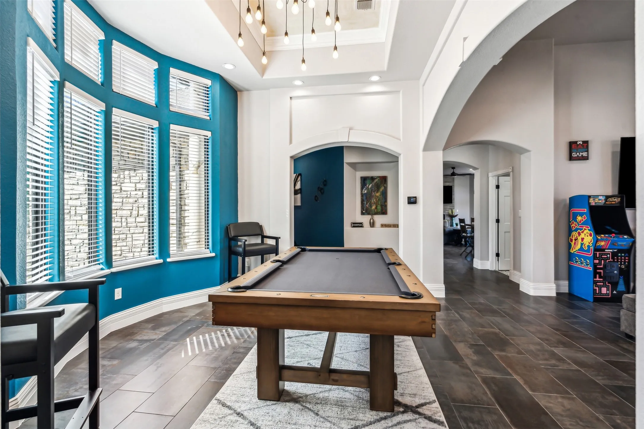 Game room featuring a billiard table, a curved wall of multiple windows with blinds, wood-finish flooring, a tray ceiling with pendant lighting, and multiple arched doorways