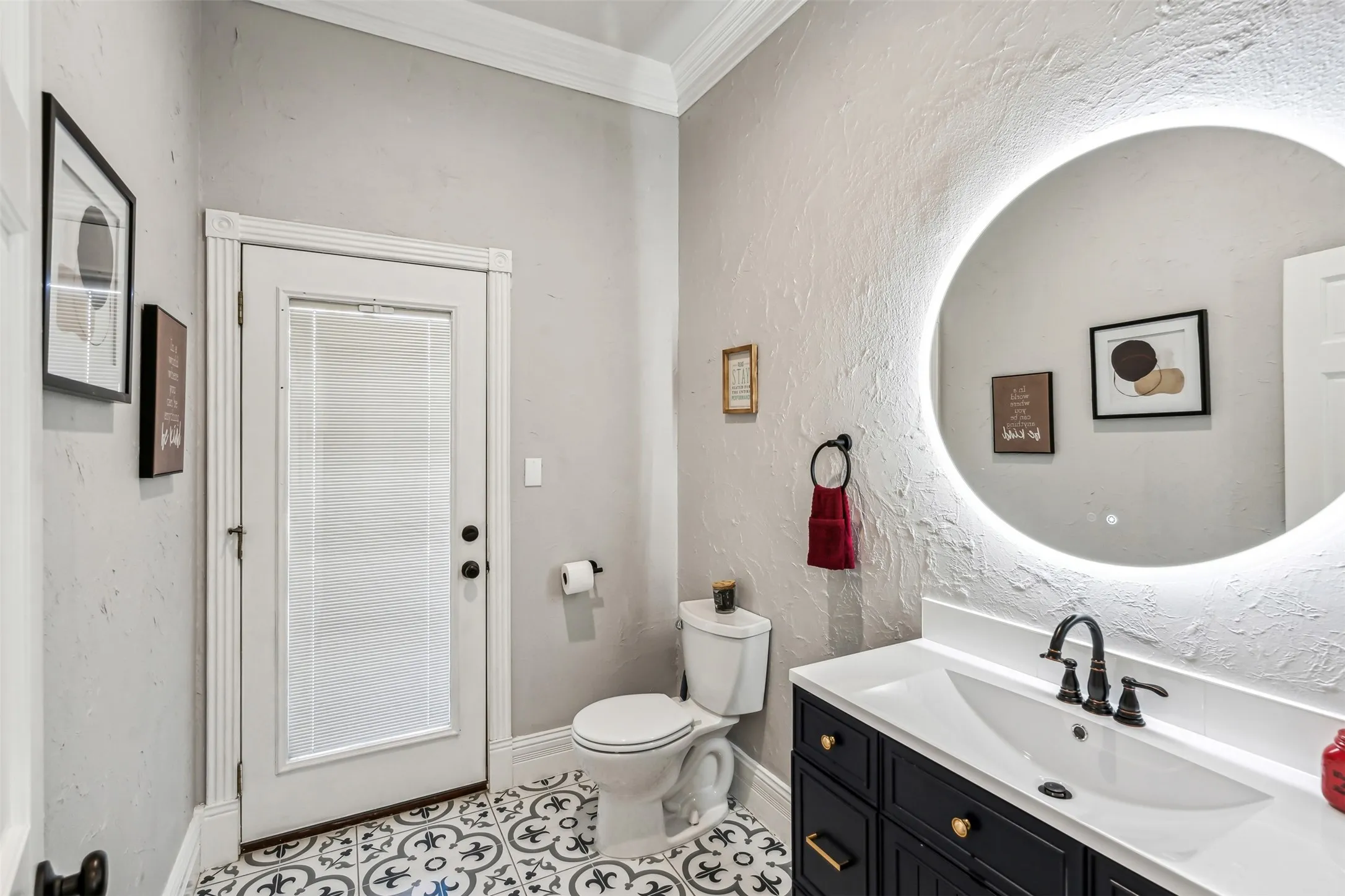 Bathroom featuring a black vanity with a white countertop and undermount sink, a circular backlit mirror, and patterned floor tiles