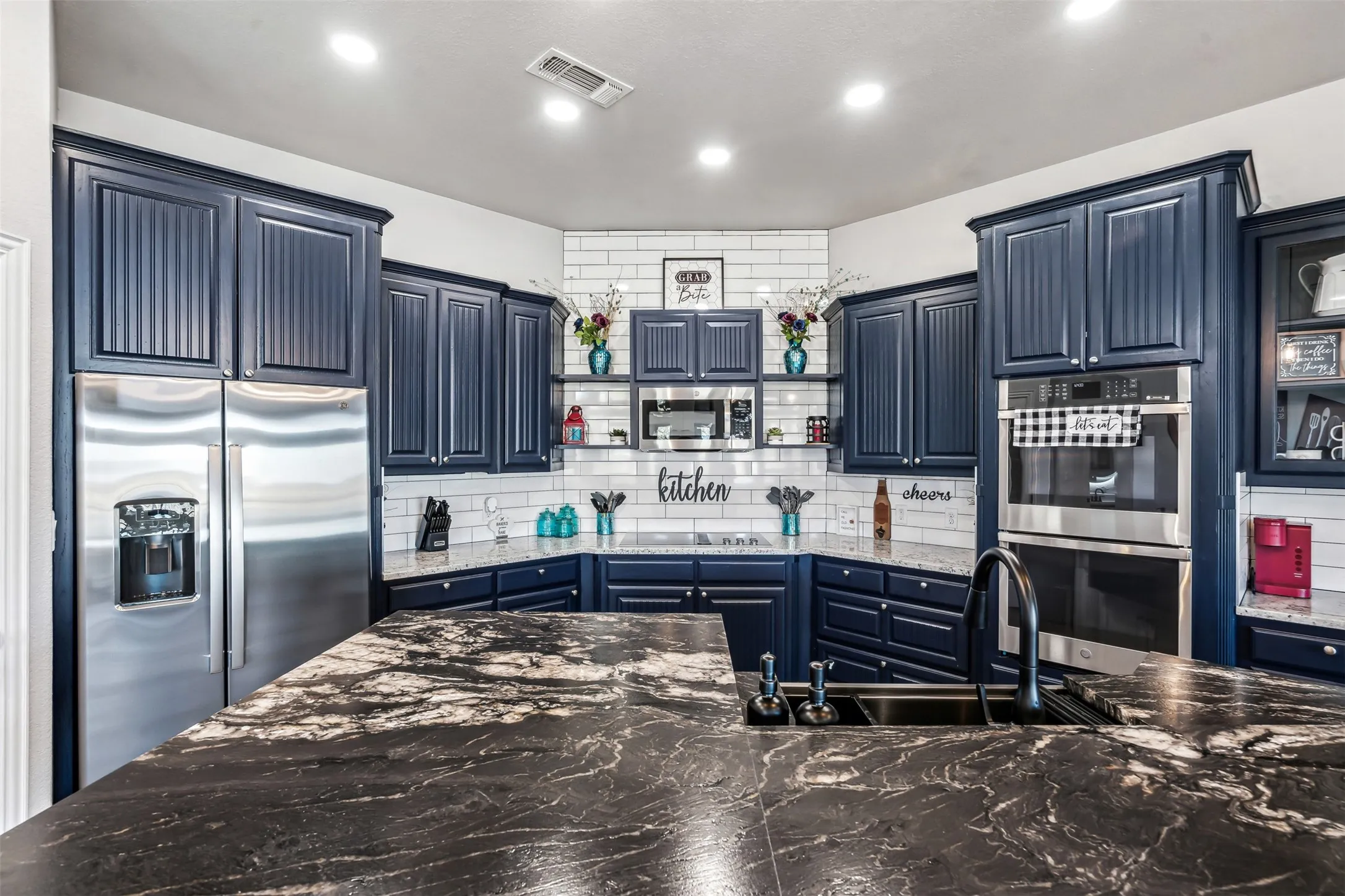Kitchen featuring dark cabinetry, stainless steel appliances, a subway tile backsplash, recessed lighting, and a kitchen island with a dark sink and faucet