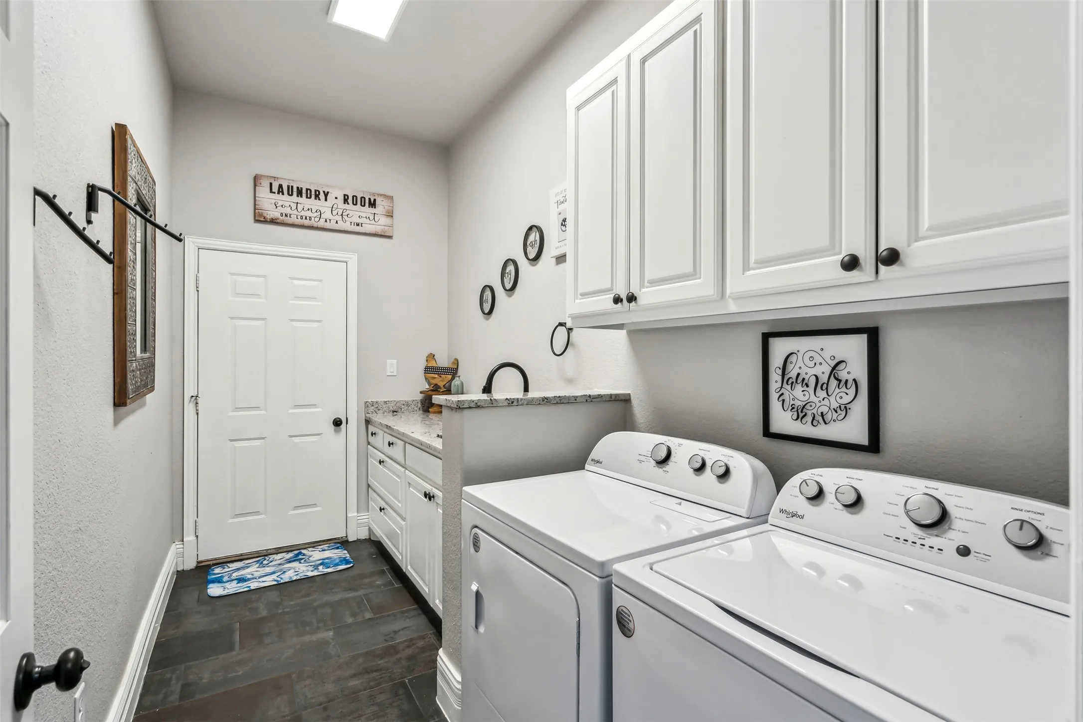 Dedicated laundry room featuring dark tile flooring, white shaker cabinetry, a granite-finish countertop with a built-in sink, and overhead recessed lighting