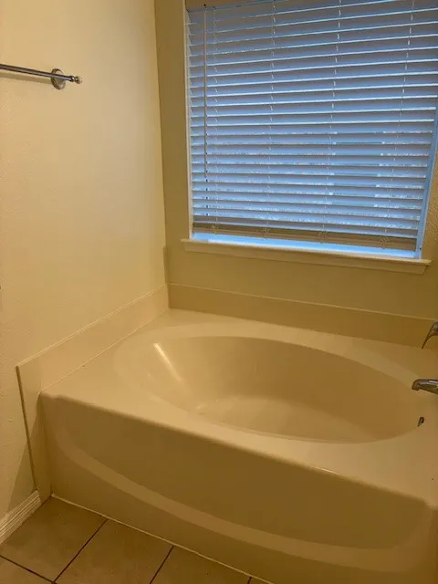 Soaking tub with integrated surround, chrome fixtures, and a window with horizontal blinds