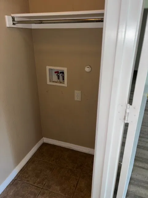 Dedicated laundry closet featuring a built-in shelf, hanging rod, water hookups, electrical outlet, and durable tile flooring
