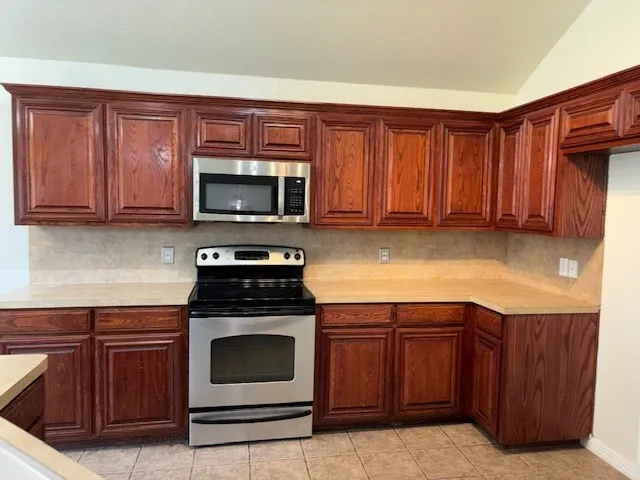 Kitchen featuring richly toned wood cabinetry, light countertops, and a tiled backsplash