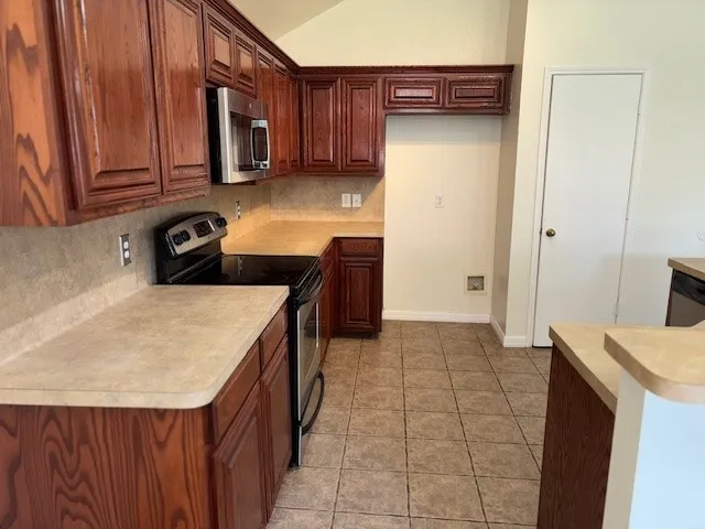 Kitchen featuring rich wood cabinetry, stainless steel microwave, black electric range, light-toned countertops, and tile flooring