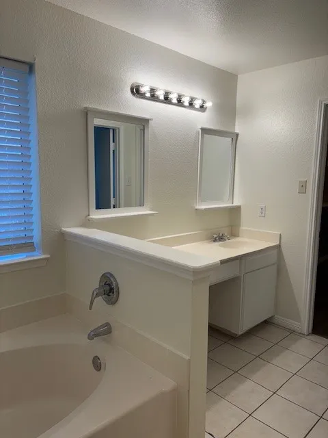 Bathroom featuring a built-in soaking tub, a dual vanity with integrated sinks, and tiled flooring