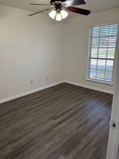 Spacious room featuring wood-finish flooring, neutral-toned walls, and a ceiling fan with integrated lighting