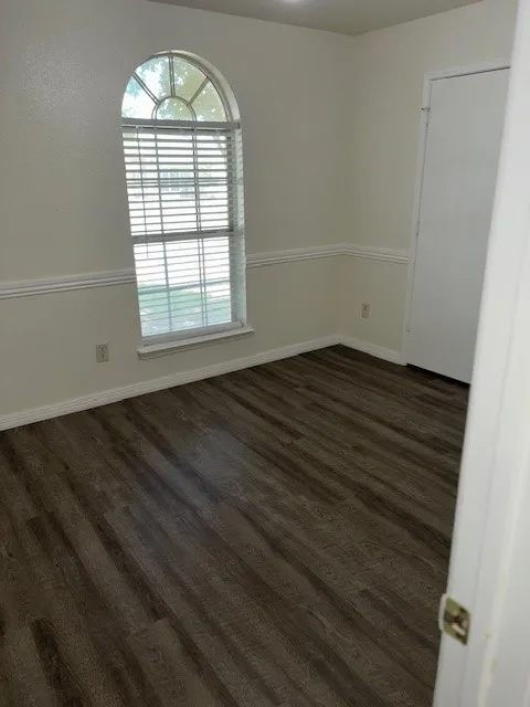 Room featuring an arched window with blinds, wood-finish flooring, white baseboards, and decorative wall trim