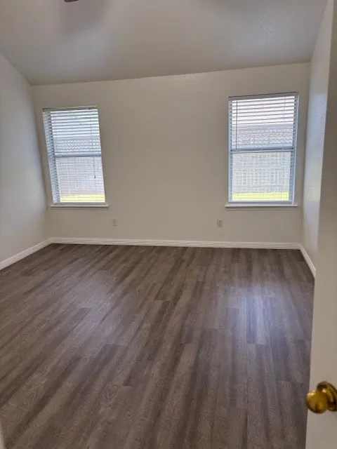 Bright room featuring two windows with horizontal blinds, wood-finish flooring, white baseboards, and neutral wall paint