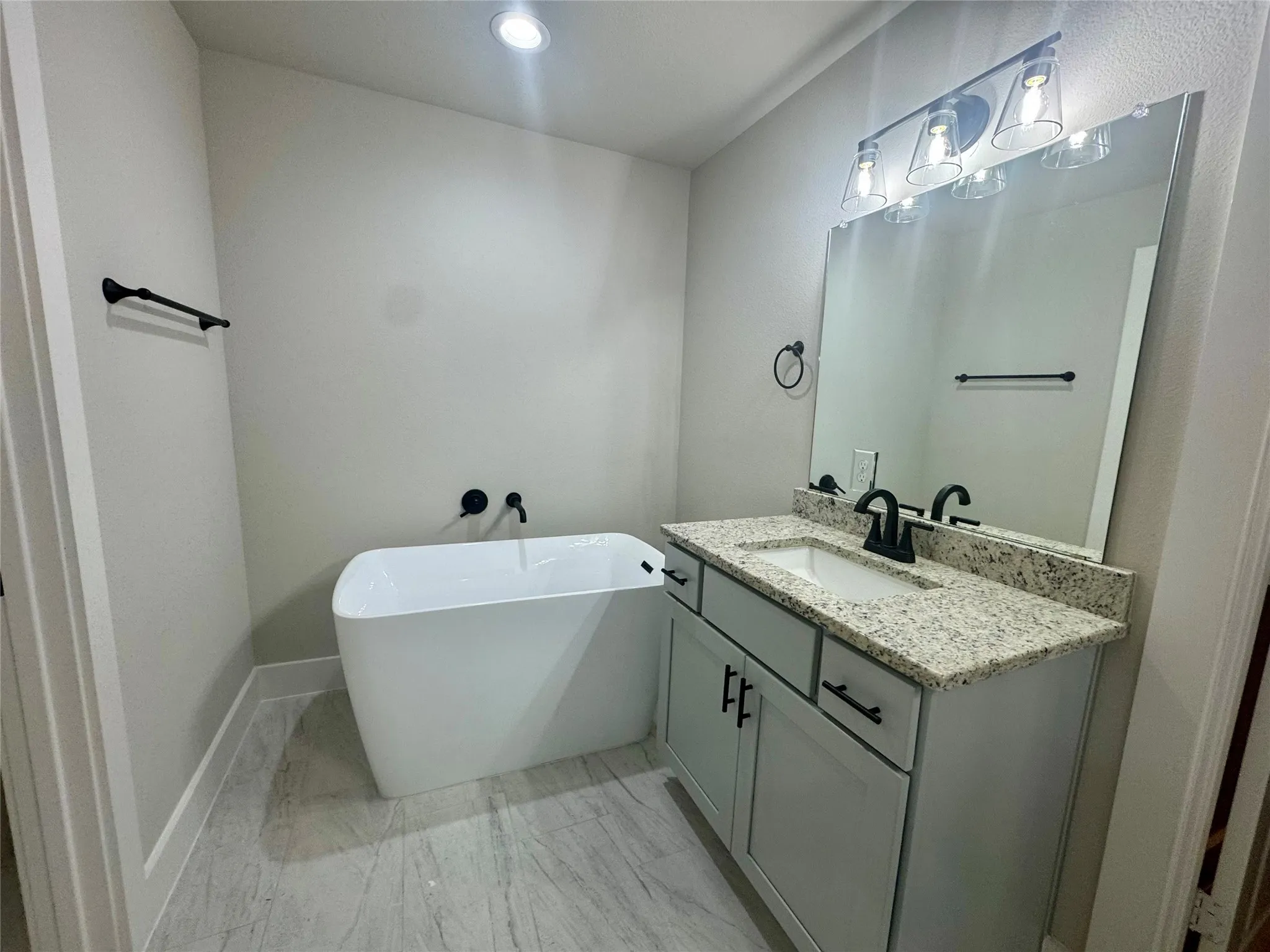 Full bathroom with a freestanding bath, vanity, marble look tiles, and recessed lighting