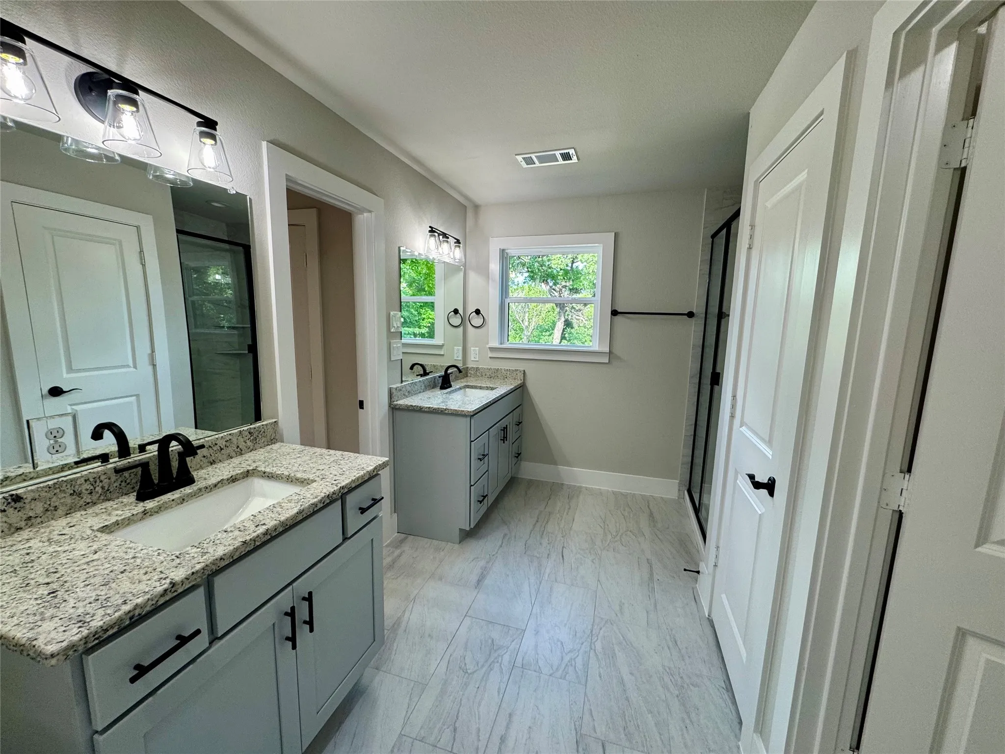 Bathroom featuring marble look tile flooring, a stall shower, and two vanities