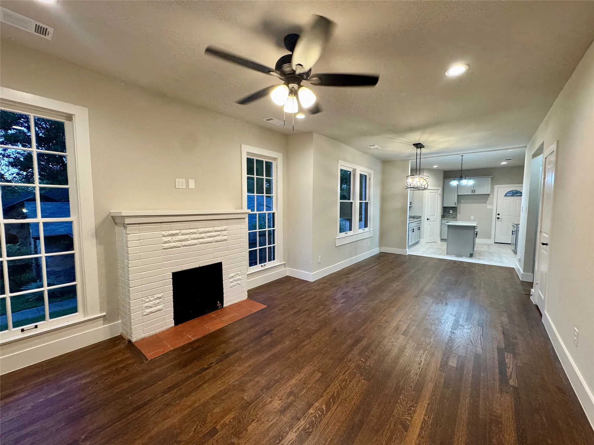 Unfurnished living room featuring dark wood-style floors, ceiling fan, a fireplace, a chandelier, and recessed lighting