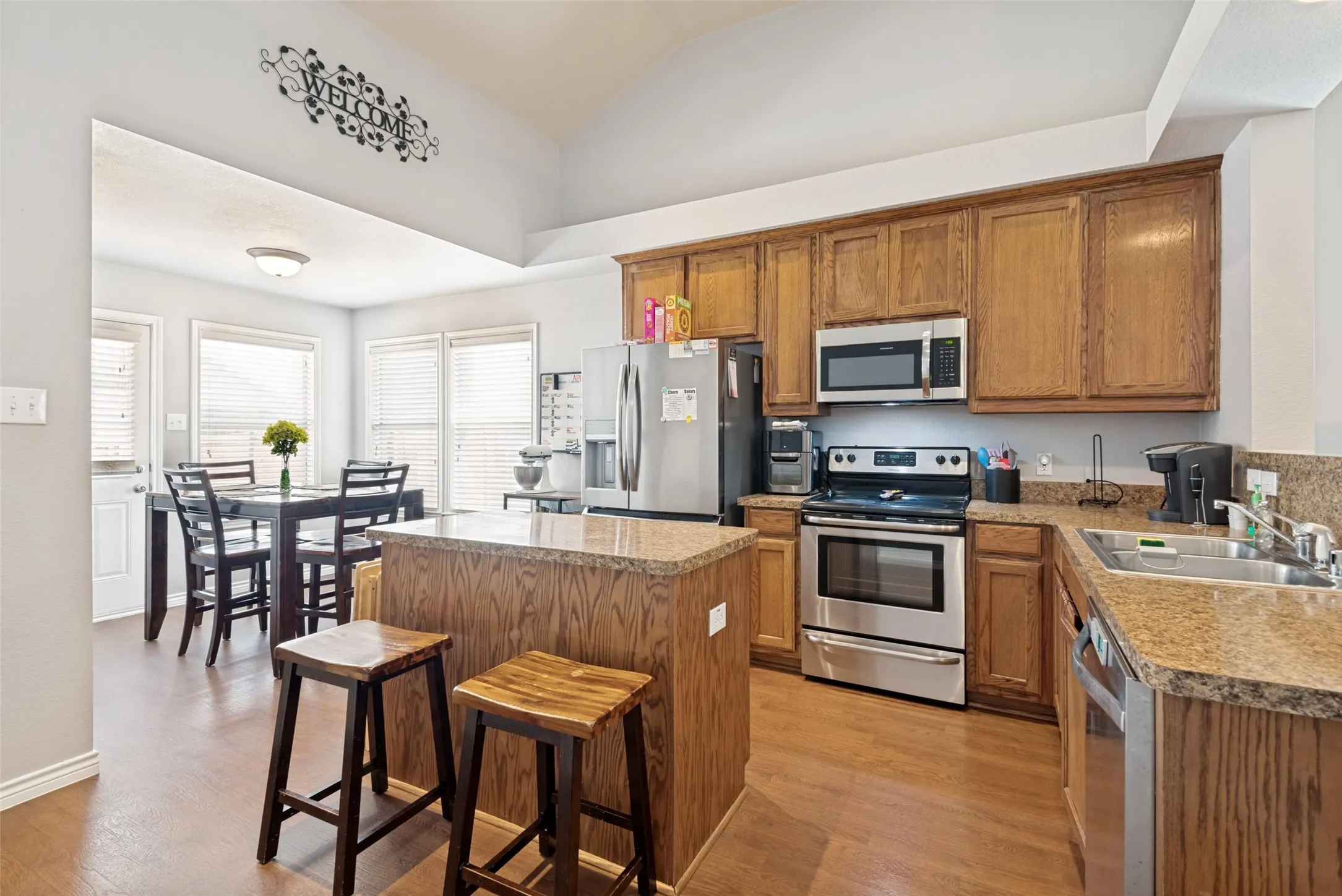 Kitchen with wood-finish flooring, warm-toned cabinetry, stainless steel appliances, and a central island with a breakfast bar