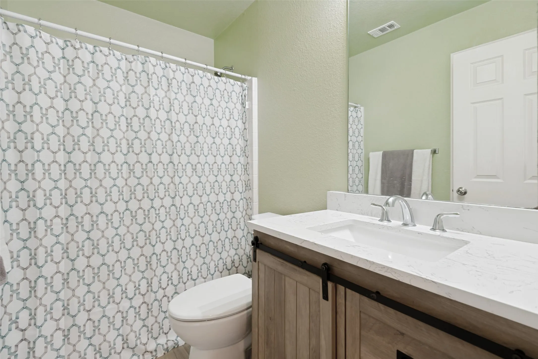 Bathroom vanity featuring a single-basin sink, light-toned countertop, and wood-finish cabinetry with barn door style hardware