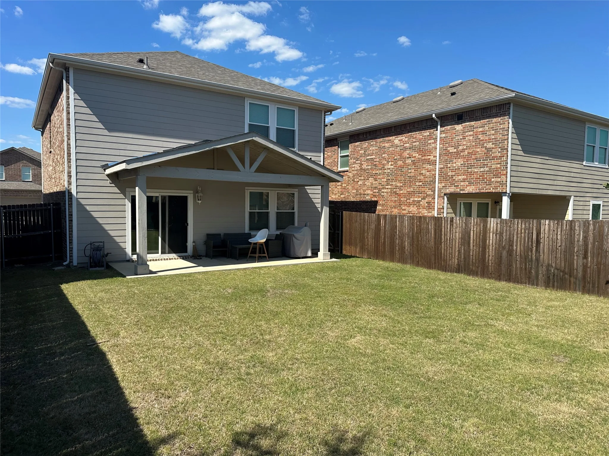 Expansive lawn with a wooden privacy fence, a covered patio with a concrete slab, and sliding glass doors leading into the residence