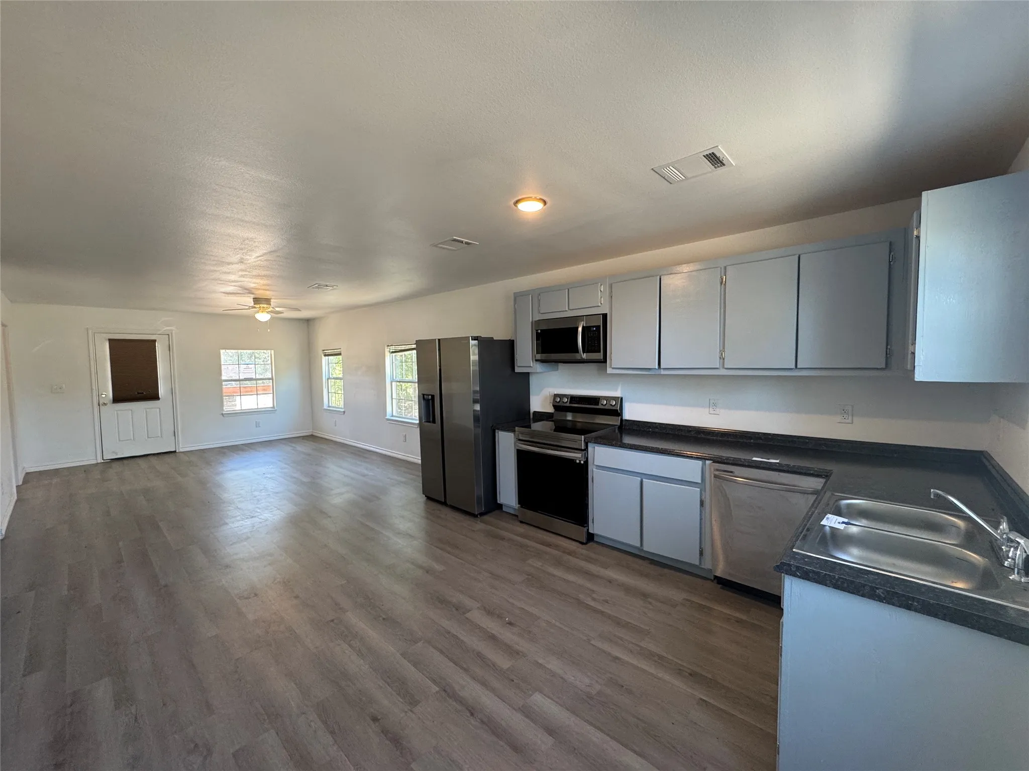 Open-concept living area featuring wood-finish flooring, a ceiling fan, and multiple windows for natural light