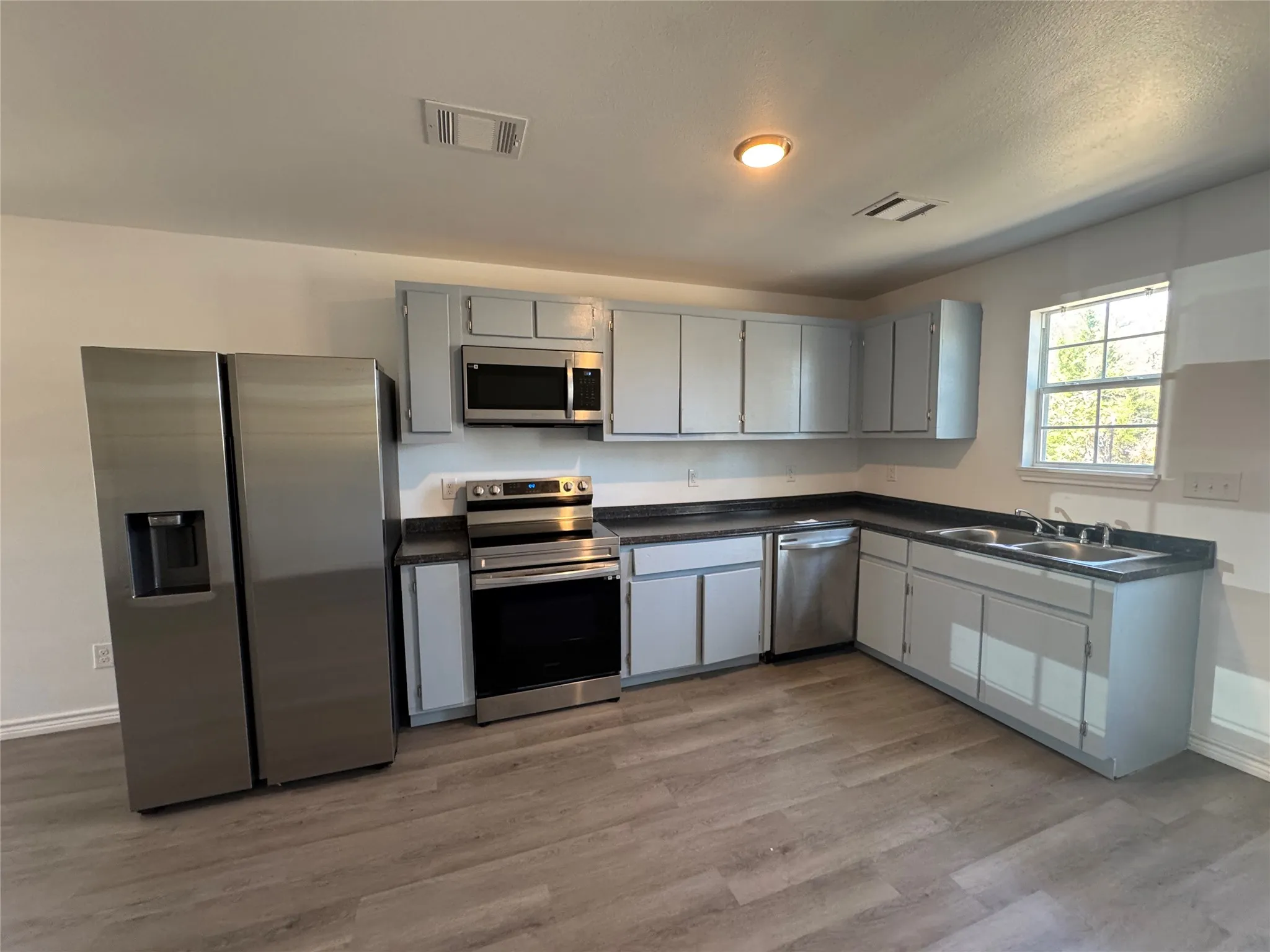 Kitchen featuring L-shaped cabinetry, dark countertops, stainless steel appliances, and wood-finish flooring