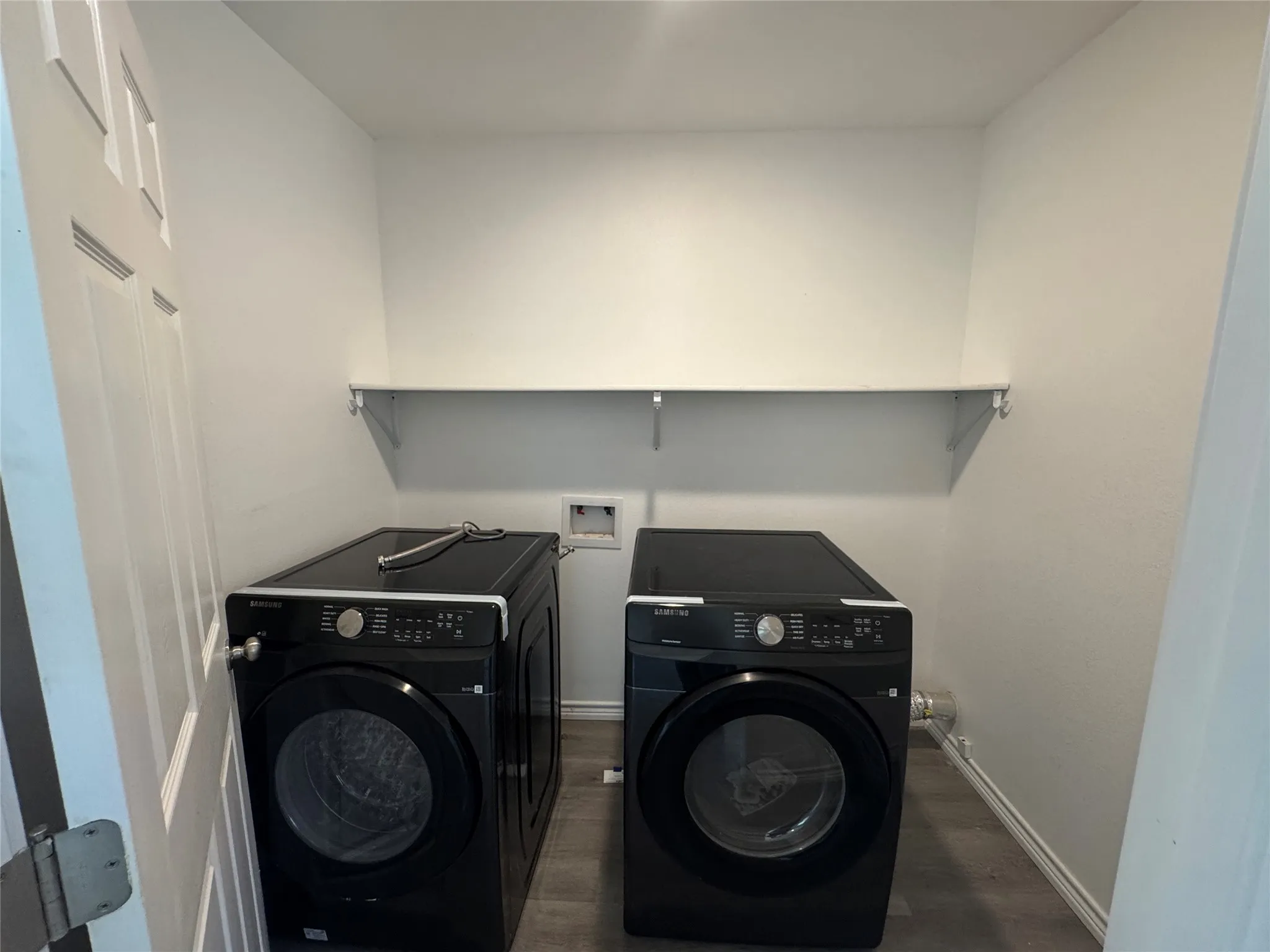 Dedicated laundry area featuring a built-in white shelf for storage, white walls, and wood-finish flooring