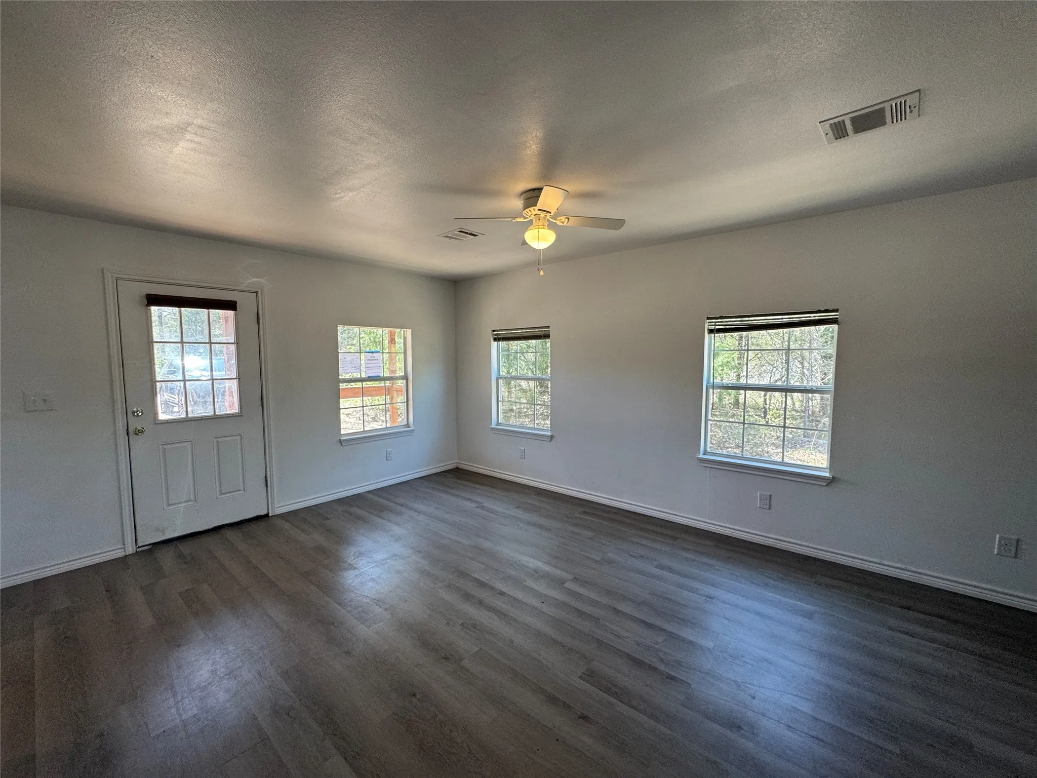 Spacious room featuring wood-finish flooring, white walls, multiple windows, and a ceiling fan with integrated lighting