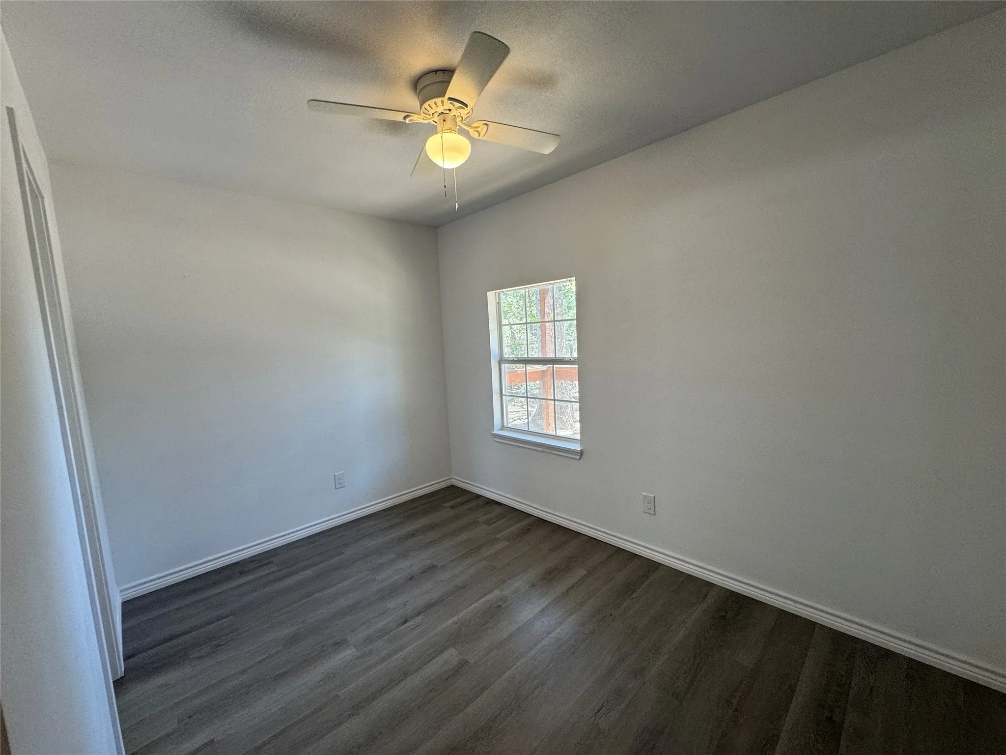 Room featuring wood-finish flooring, white walls, and a ceiling fan with integrated lighting