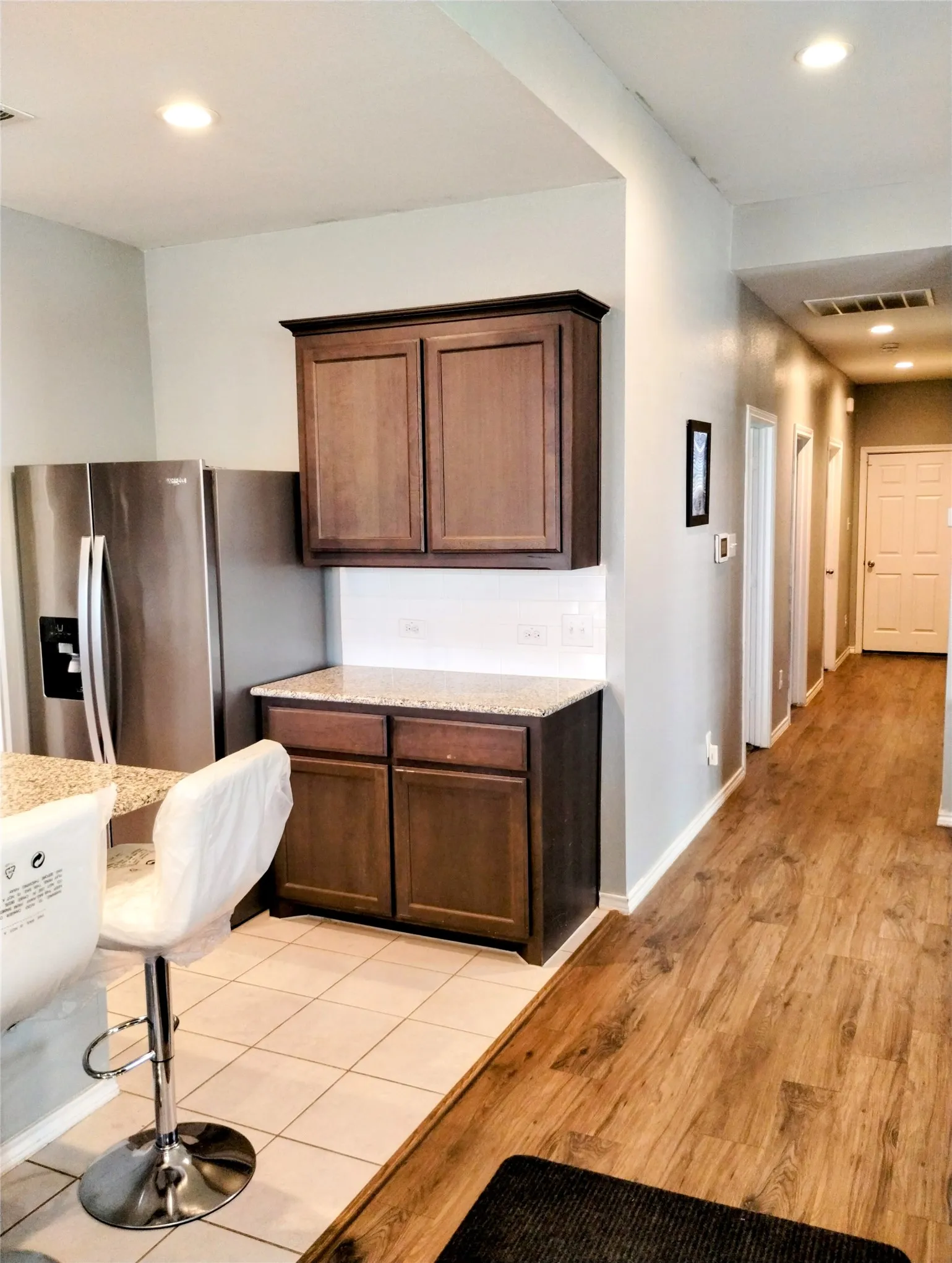 Kitchen featuring light wood-type flooring, dark brown cabinetry, stainless steel fridge with ice dispenser, and light stone counters