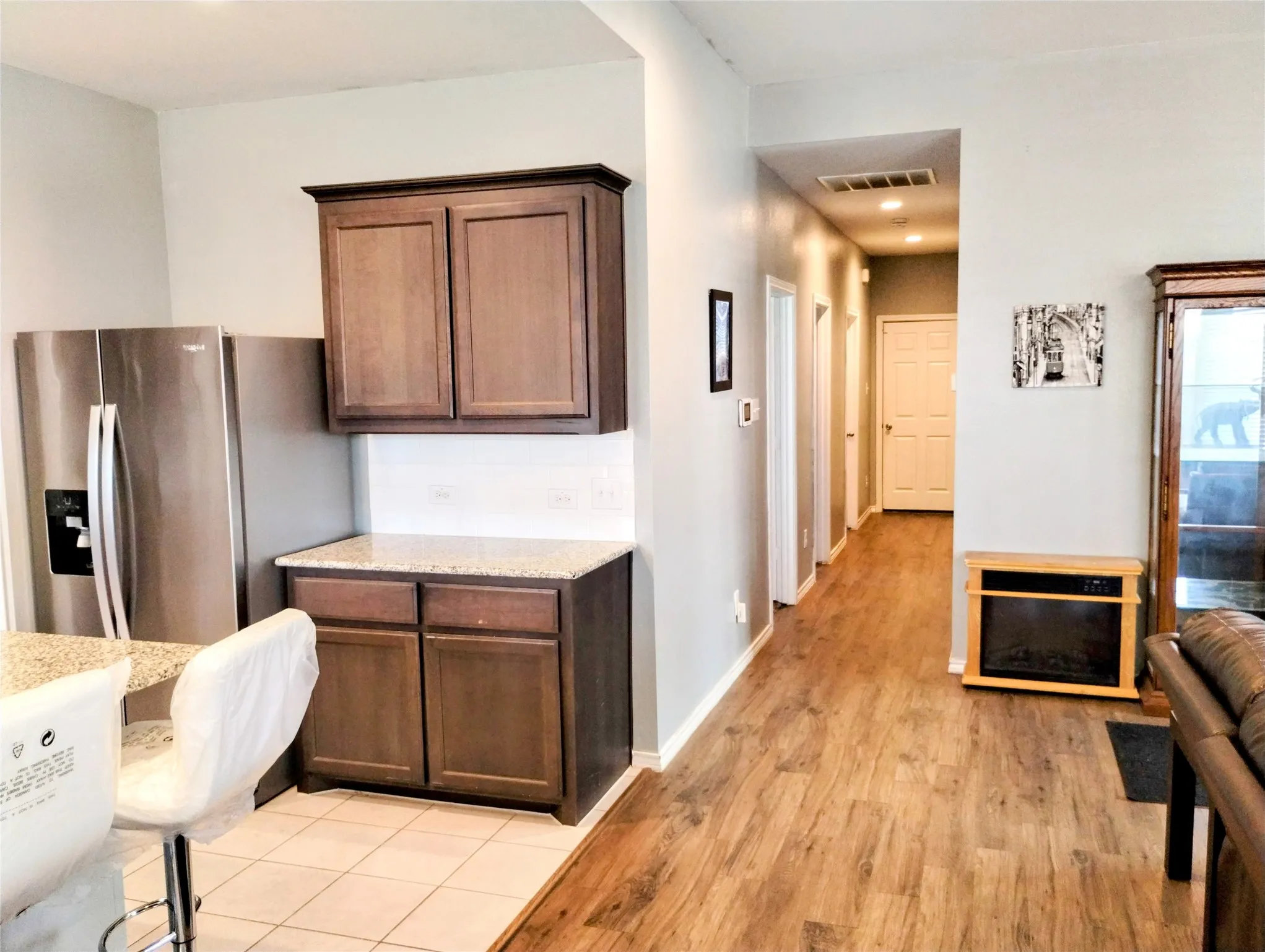 Kitchen with dark brown cabinets, light hardwood / wood-style floors, light stone countertops, and stainless steel fridge