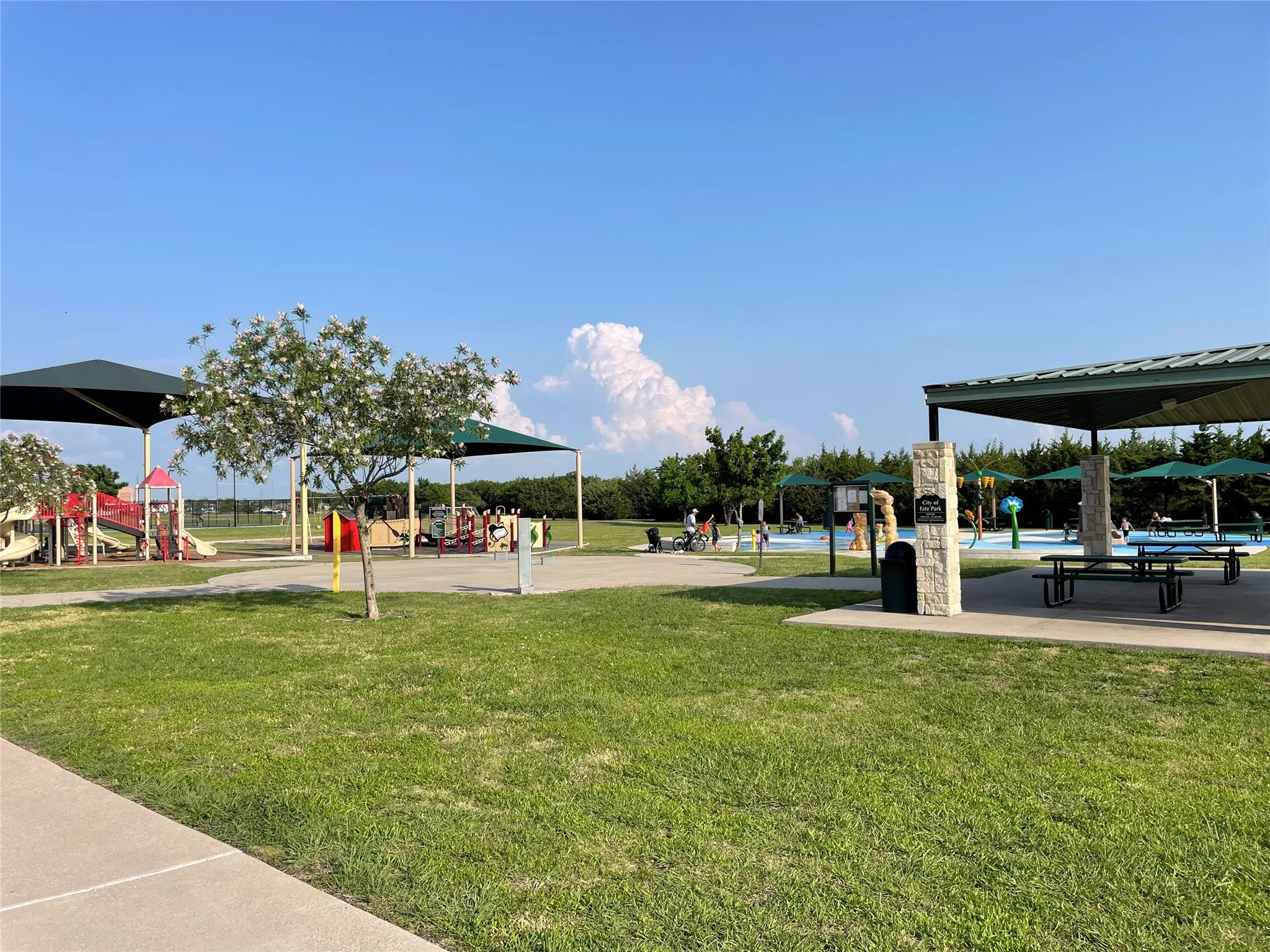 Nearest Playground, Splash Park and Covered Picnic Area. Path Through the Trees in the Background Has a Frisbee Golf Course.
