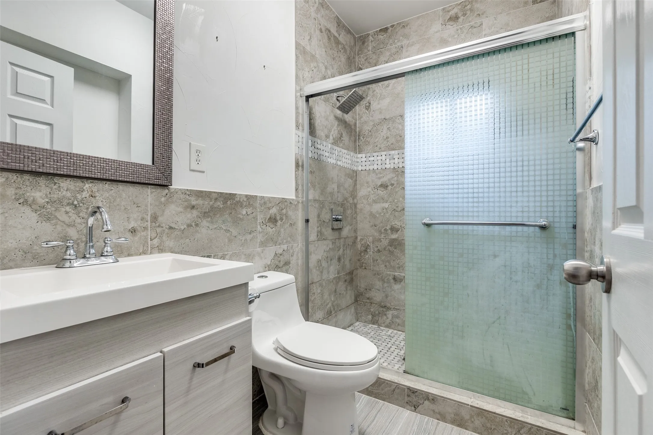 Shower with sliding frosted glass door, complemented by a mosaic tile accent strip