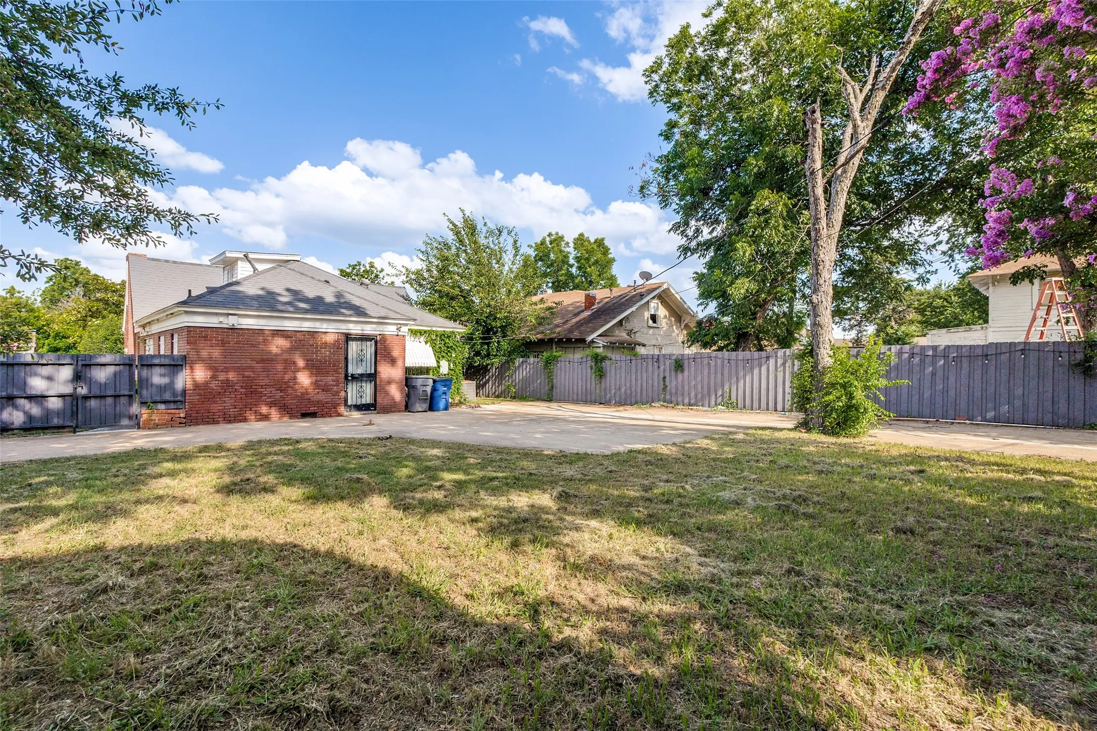 Expansive lawn area with a brick-clad building, mature trees, and privacy fencing