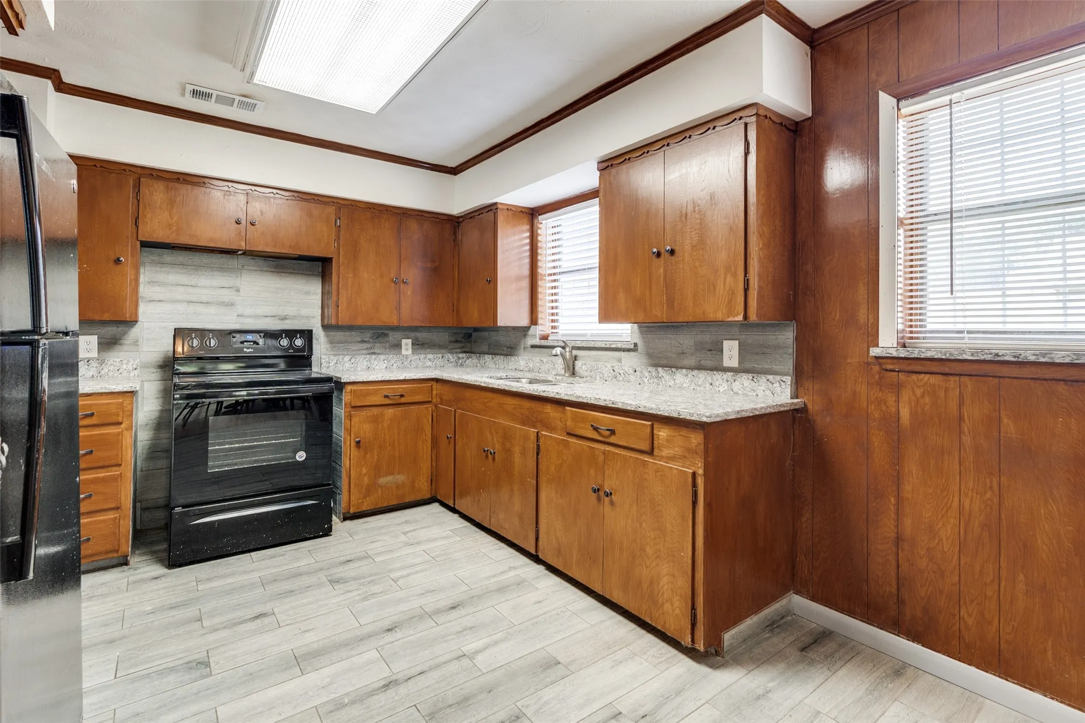 Kitchen featuring wood-finish cabinetry, granite-style countertops, a tile backsplash, and light wood-finish flooring