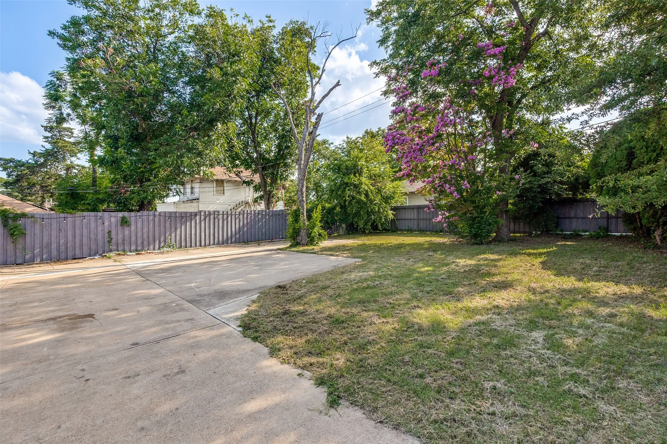 Spacious concrete area alongside a grassy yard, partially enclosed by a wooden privacy fence