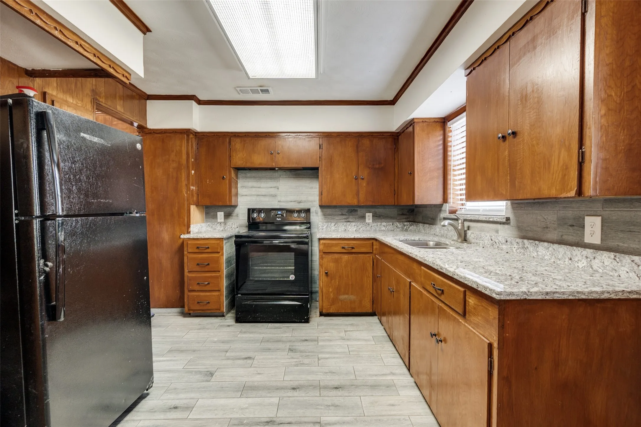 Kitchen featuring wood cabinetry, light-toned countertops, a stainless steel sink with a chrome faucet, light wood-finish flooring, and a tile backsplash
