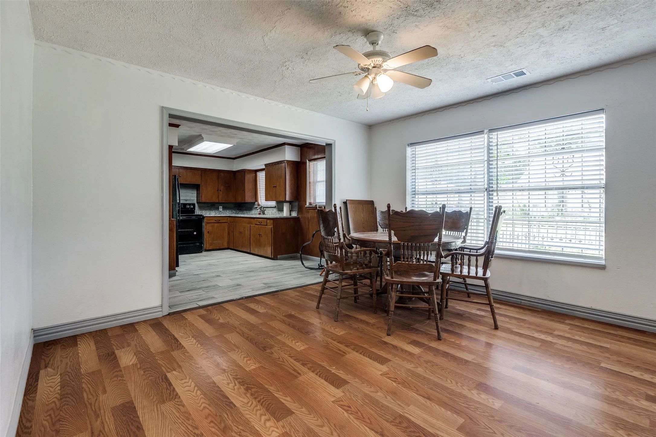 Dining area featuring wood-finish flooring, a ceiling fan with light fixture, and two large windows with horizontal blinds