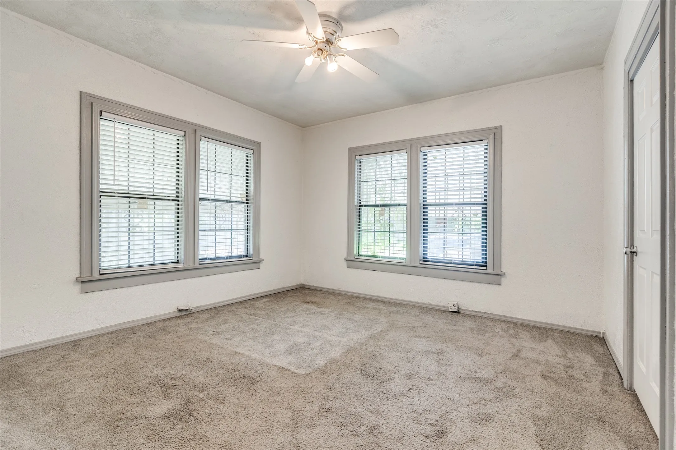 Carpeted room featuring dual windows with blinds, a ceiling fan with integrated lighting, and a white interior door