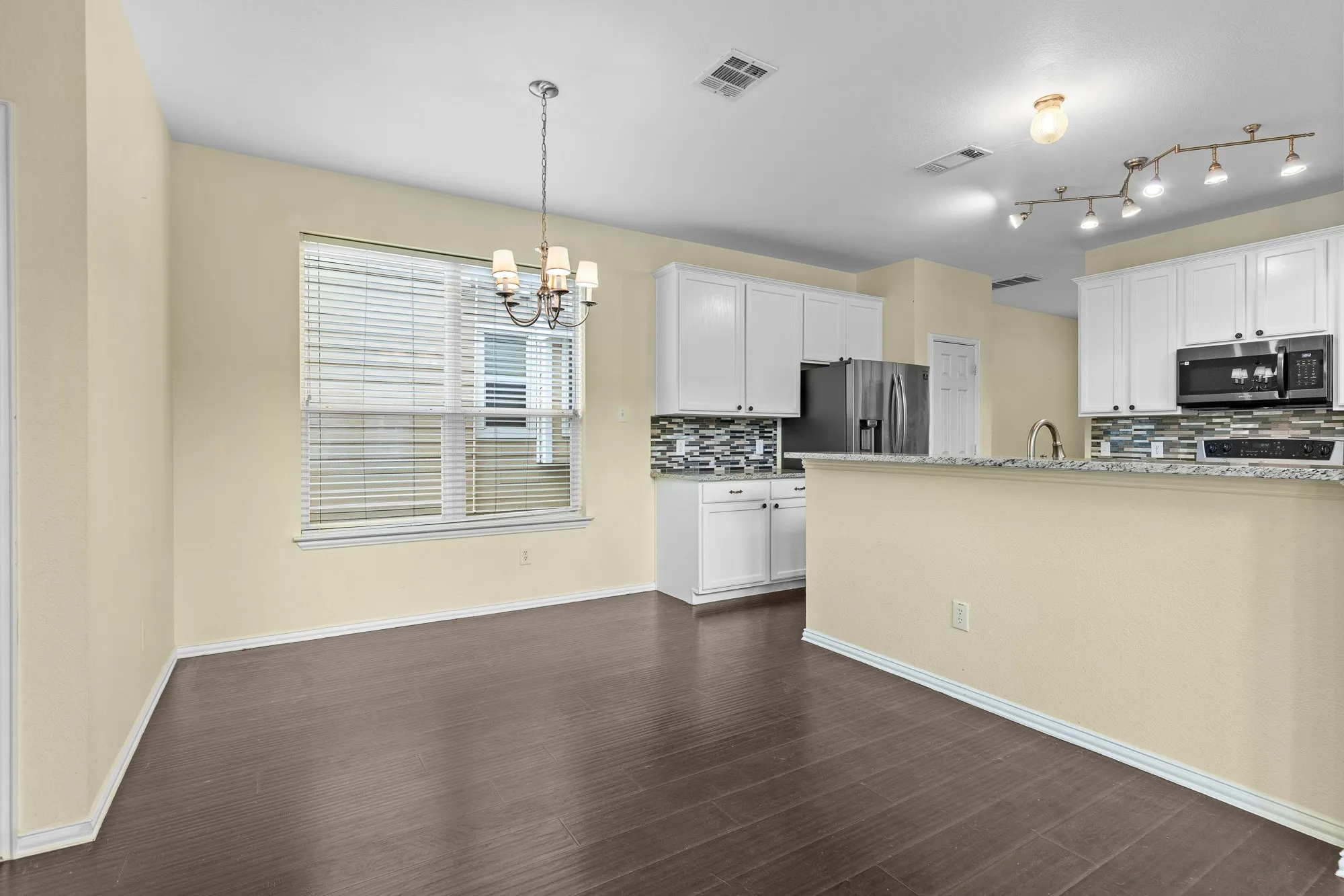 Open-concept kitchen and dining area featuring wood-finish flooring, white cabinetry, a decorative tile backsplash, and track lighting