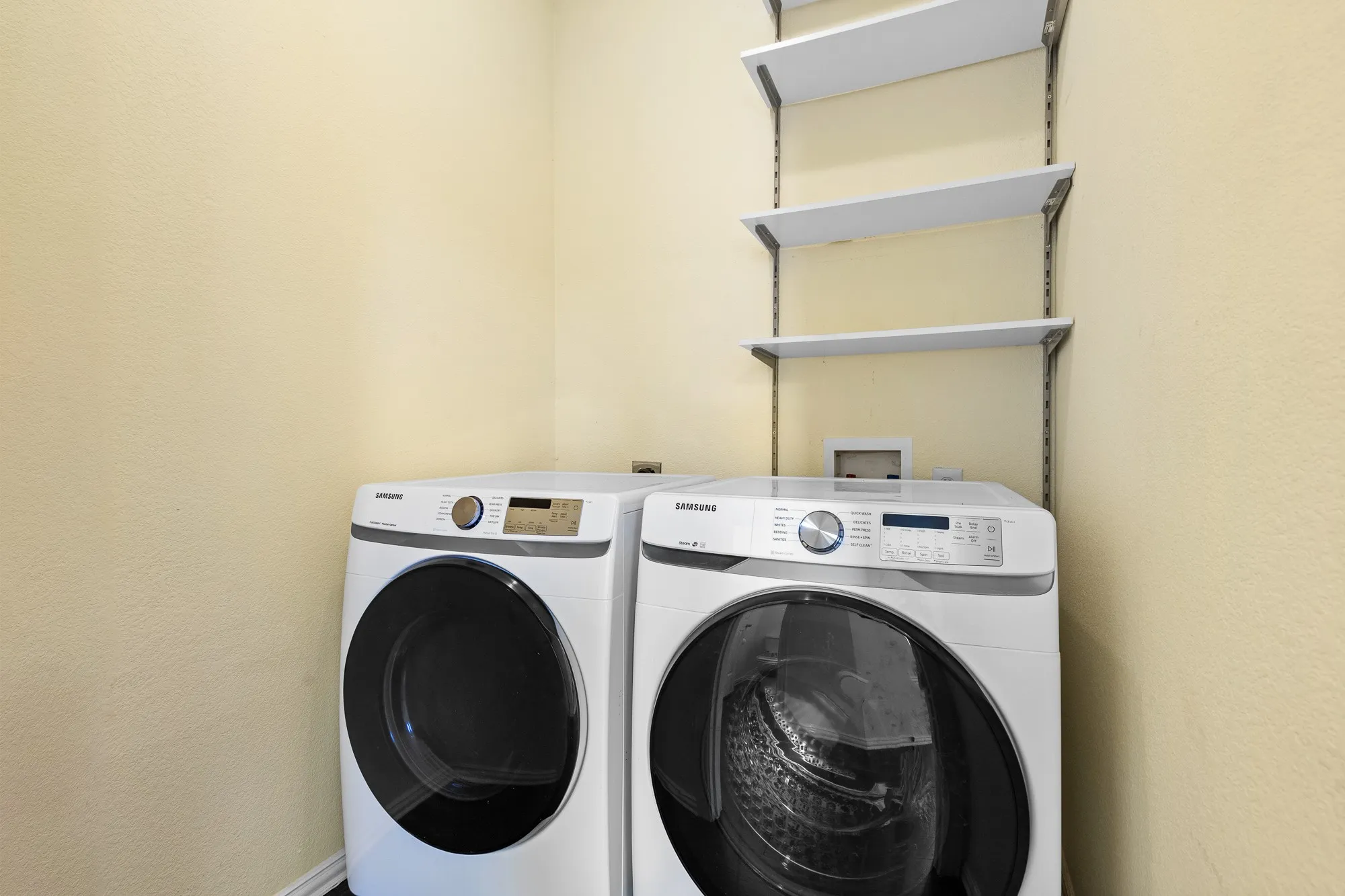 Dedicated laundry area featuring front-loading appliances and wall-mounted shelving for storage