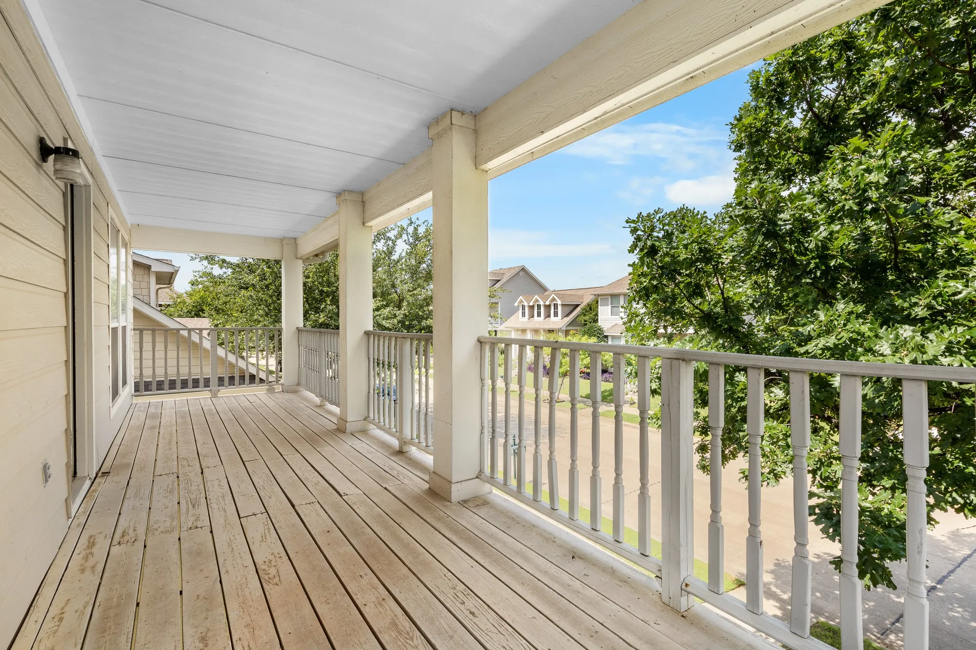 Expansive covered balcony featuring wood decking, painted balusters, and substantial support columns