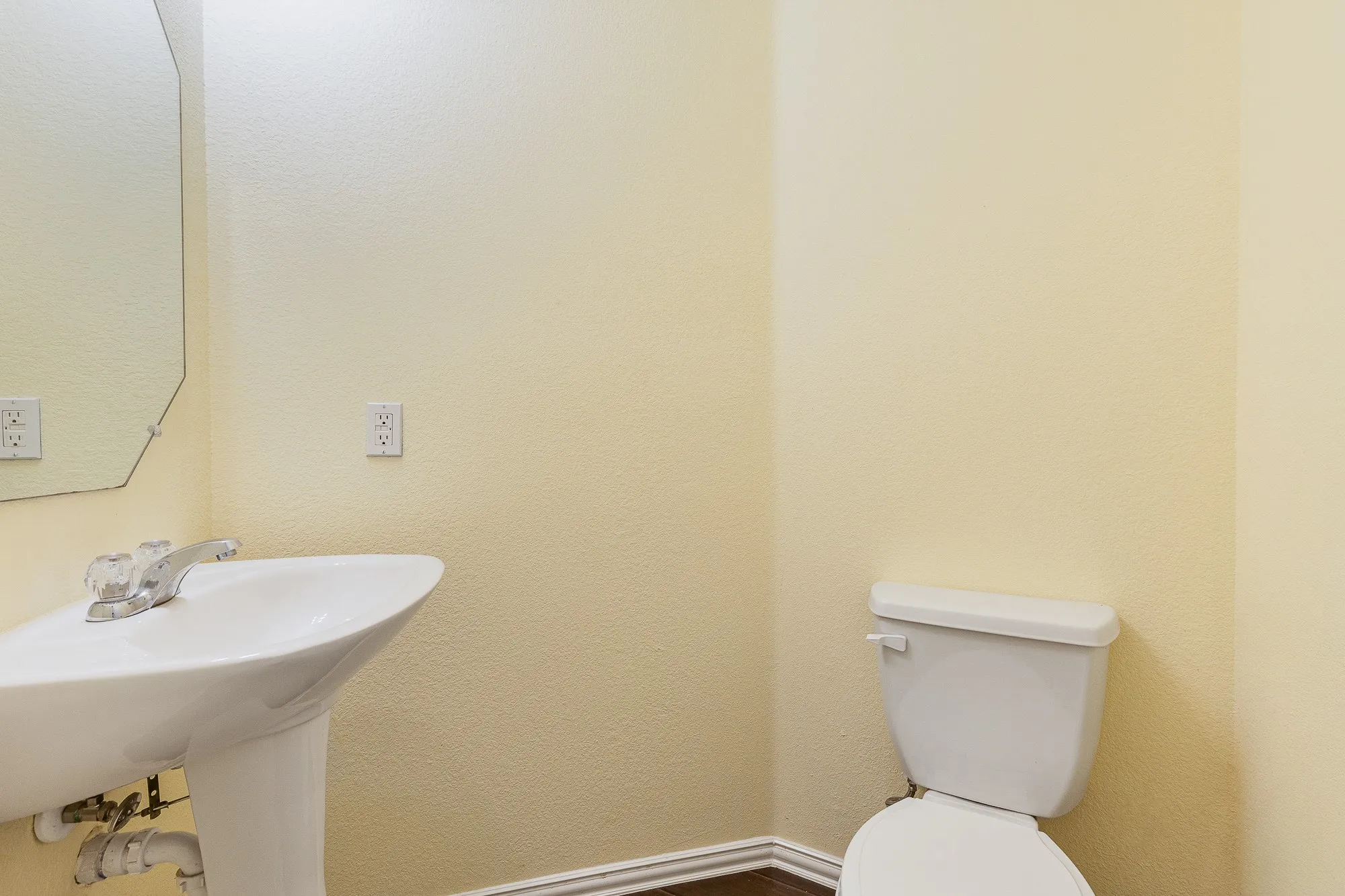 Downstairs half bath with Pedestal sink with chrome faucet, octagonal wall mirror, and neutral wall paint