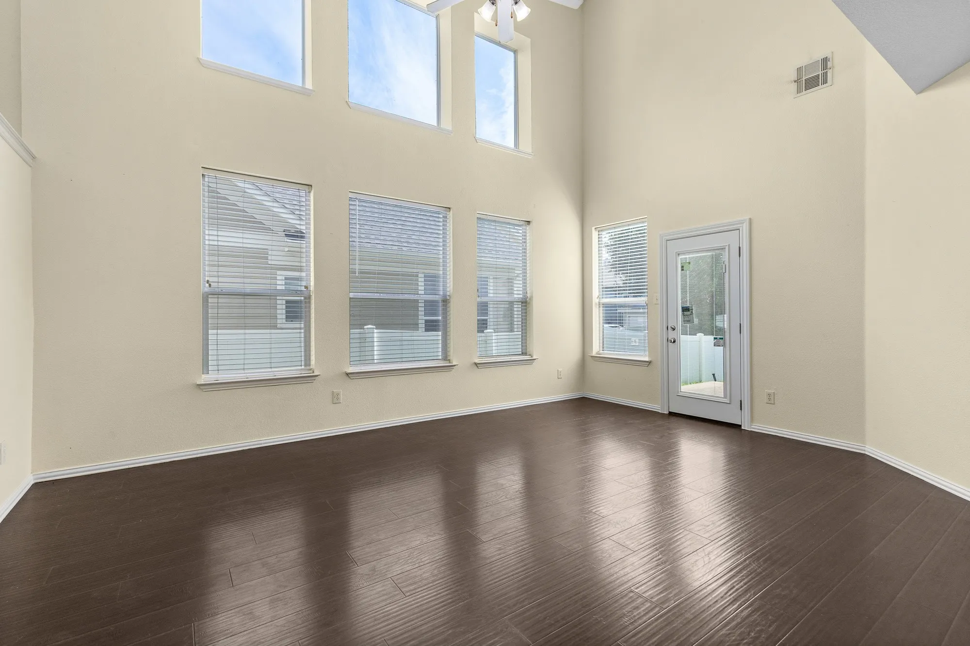 Spacious interior featuring high ceilings, wood-finish flooring, multiple large windows with blinds, a ceiling fan, and a glass-paneled exterior door