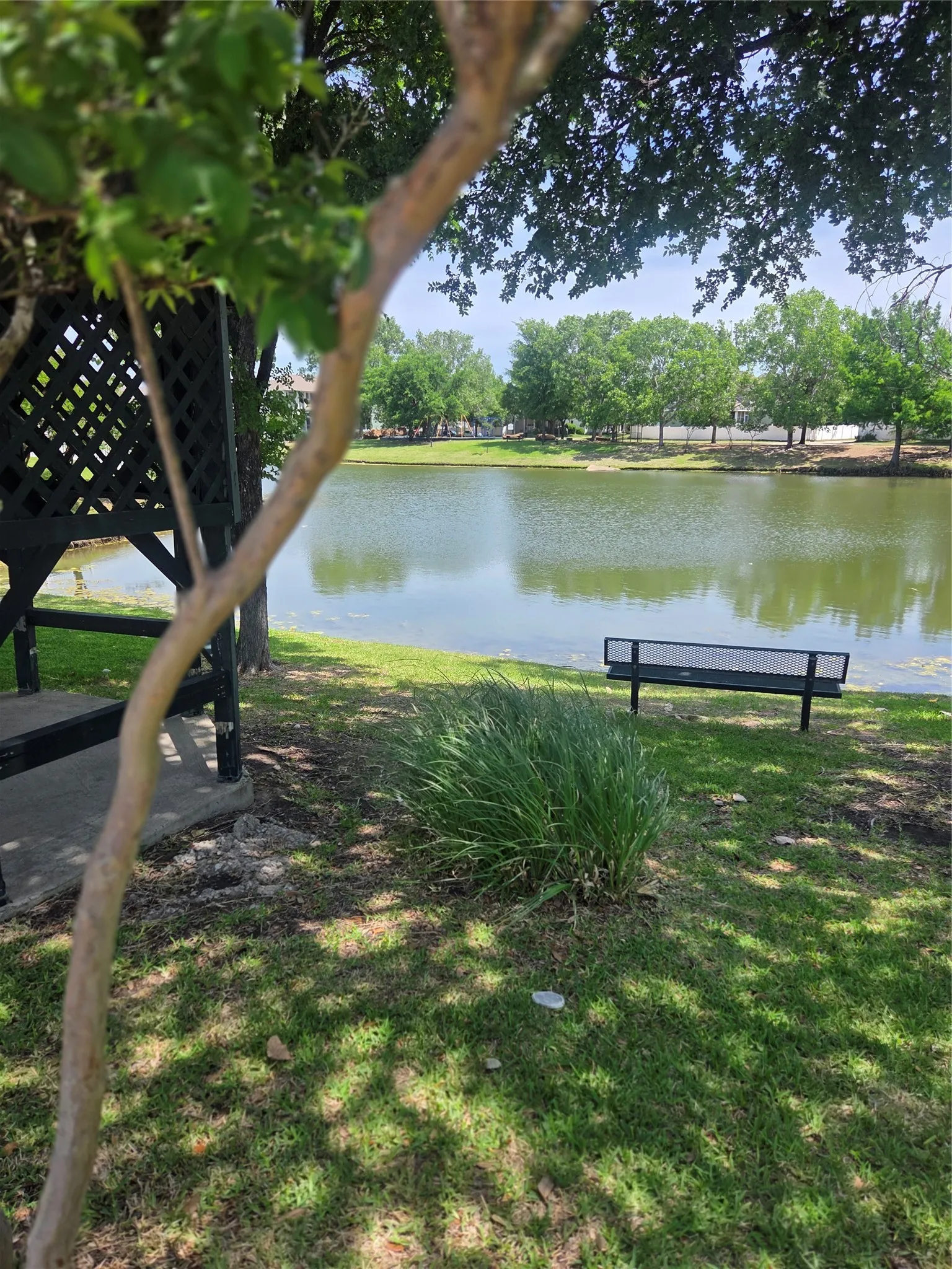 Park nearby with lake setting featuring a dark-toned gazebo with lattice detailing, a manicured lawn, and a black slatted bench