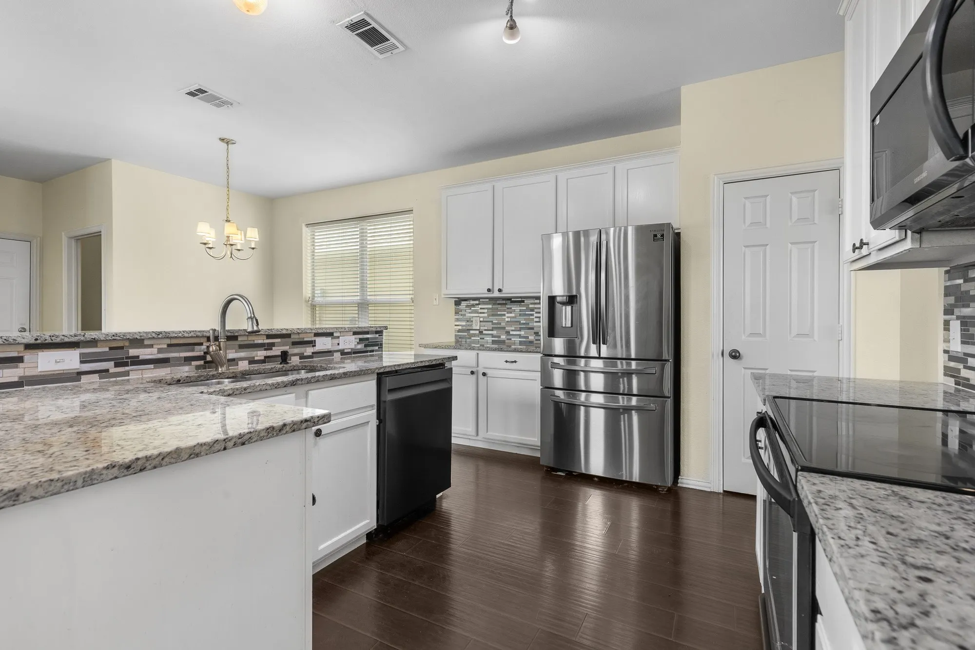 Kitchen featuring granite countertops, stainless steel appliances, dark wood-finish flooring, white cabinetry, and a mosaic tile backsplash